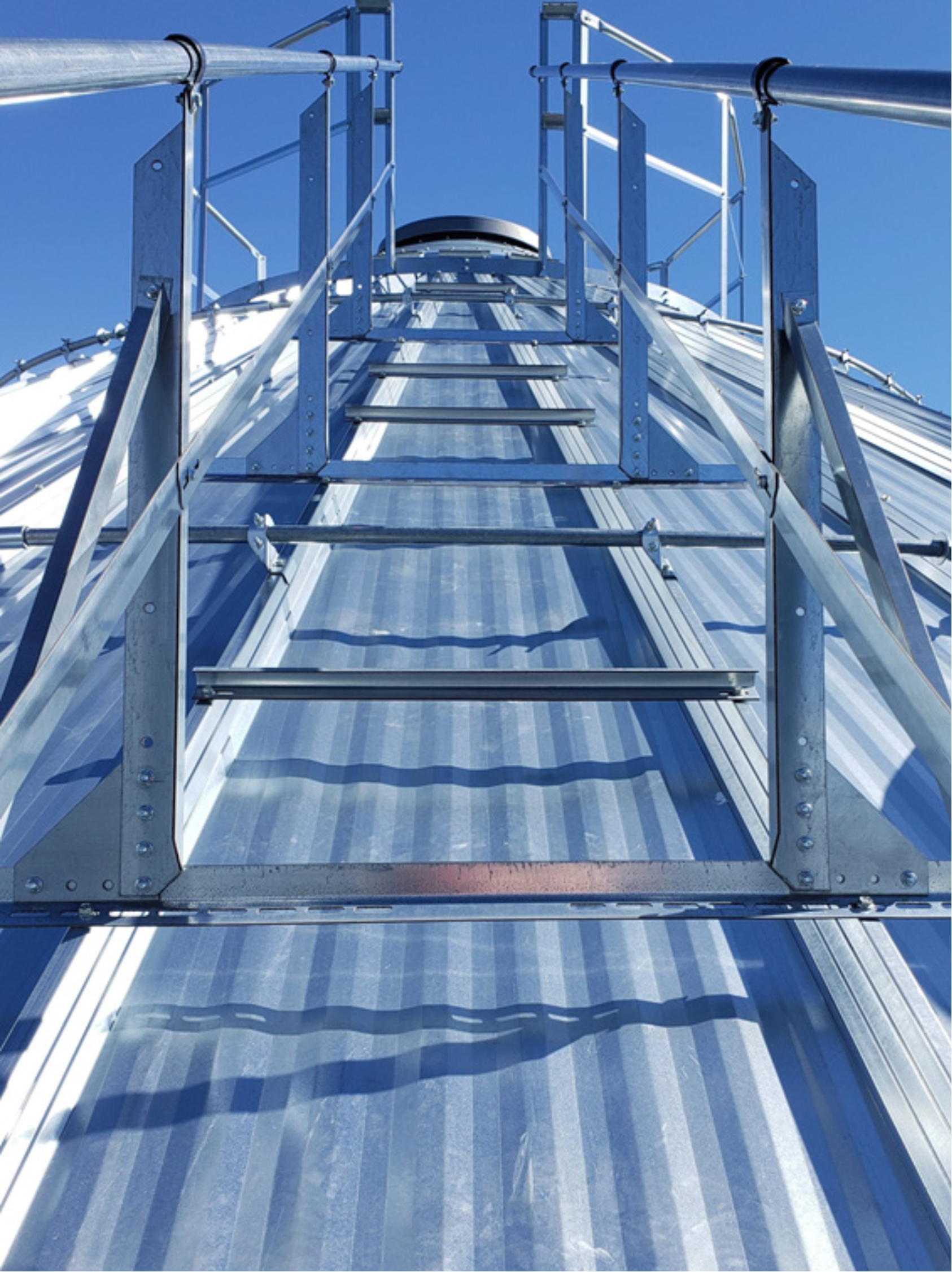 Close-up view looking up a grain bin roof ladder handrail toward the peak guardrail