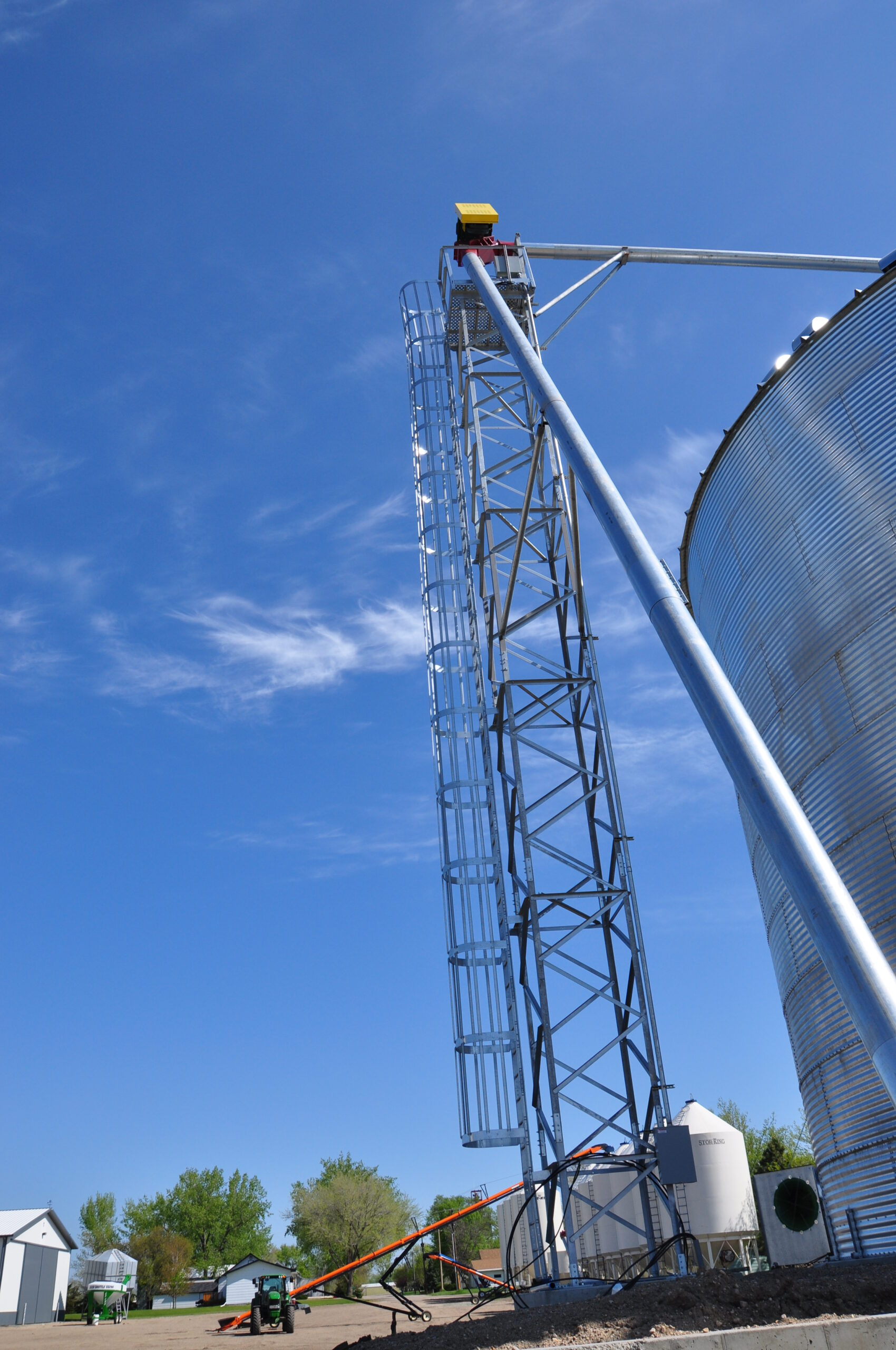 Caged ladder on a grain leg tower with auger and grain bins in the background